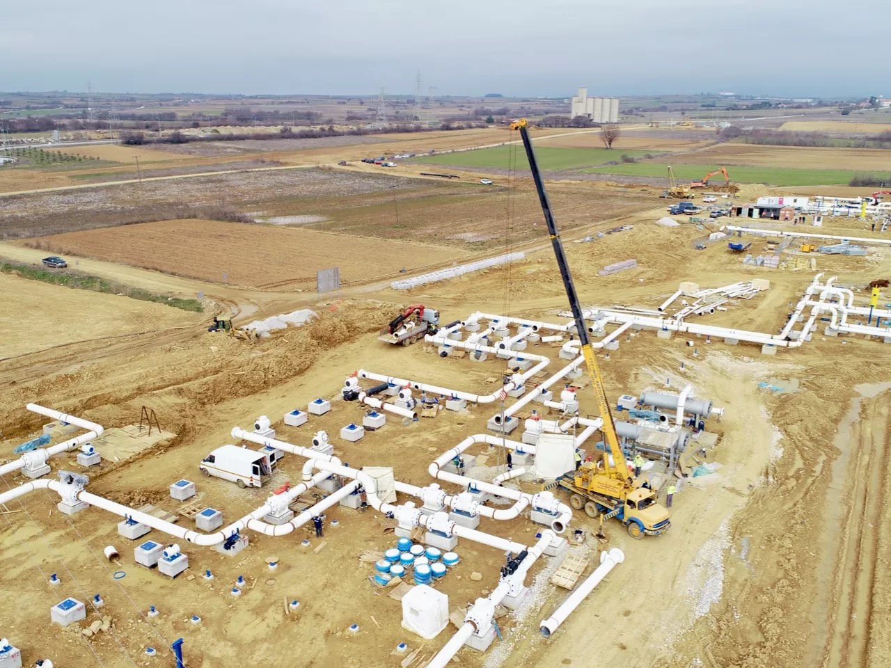 Aerial view of a station under construction: above-ground piping and a mobile crane on site