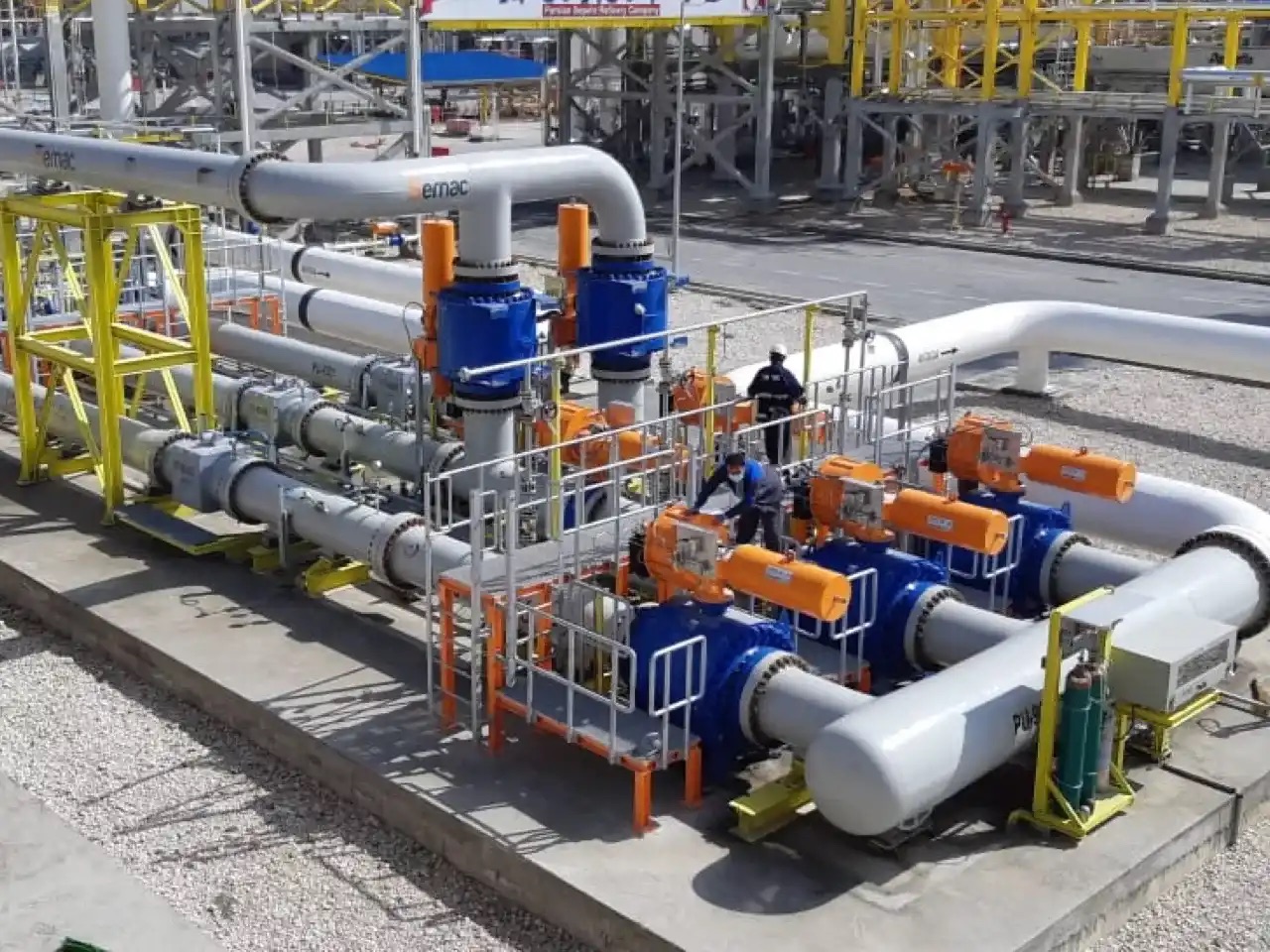 Technicians on the platform of an outdoor installation, among piping, valves and valve actuators